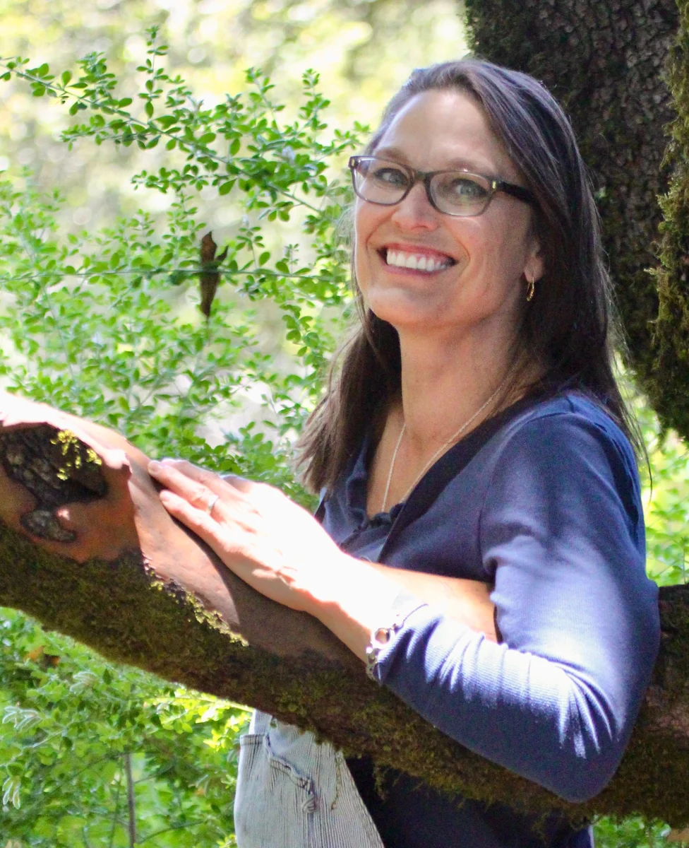 Patty smiling beside a tree in the sunlit redwoods